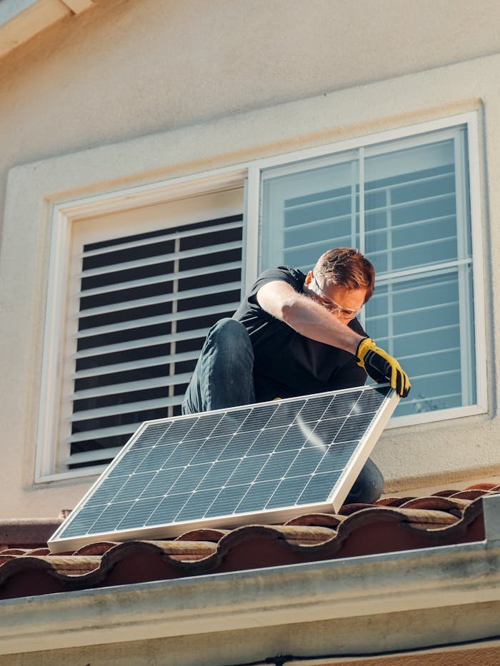 Home Man installing a solar panel on a residential rooftop, promoting sustainable energy.