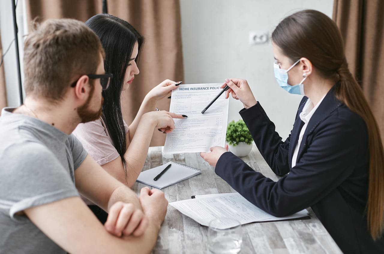About Three adults discuss a home insurance policy at a meeting table indoors.