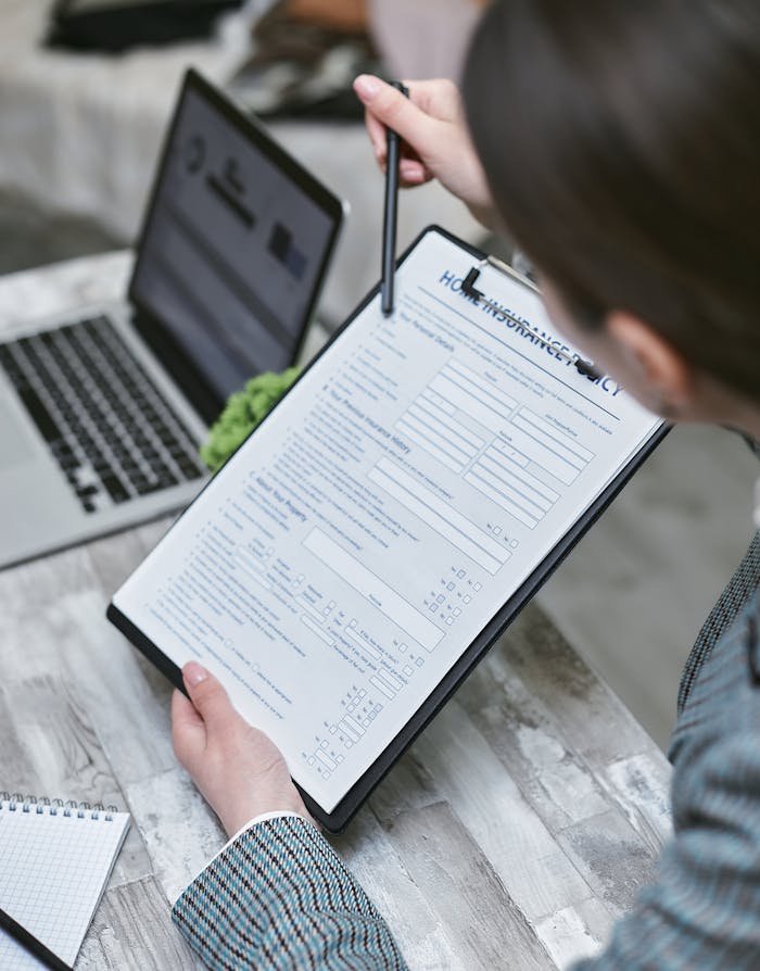 Offerings An adult reviews a home insurance policy document at a desk with a pen and laptop.